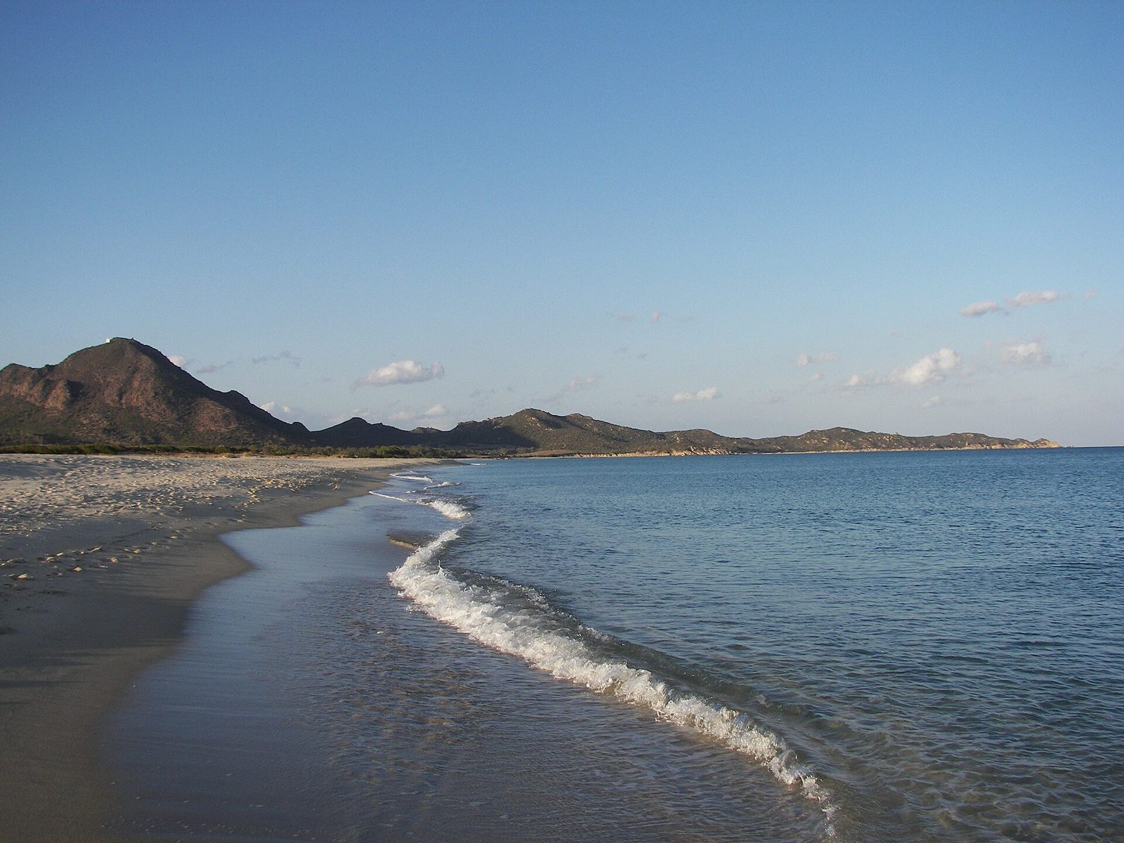 Lunga spiaggia di Costa Rei con onde sulla battigia e colline sullo sfondo