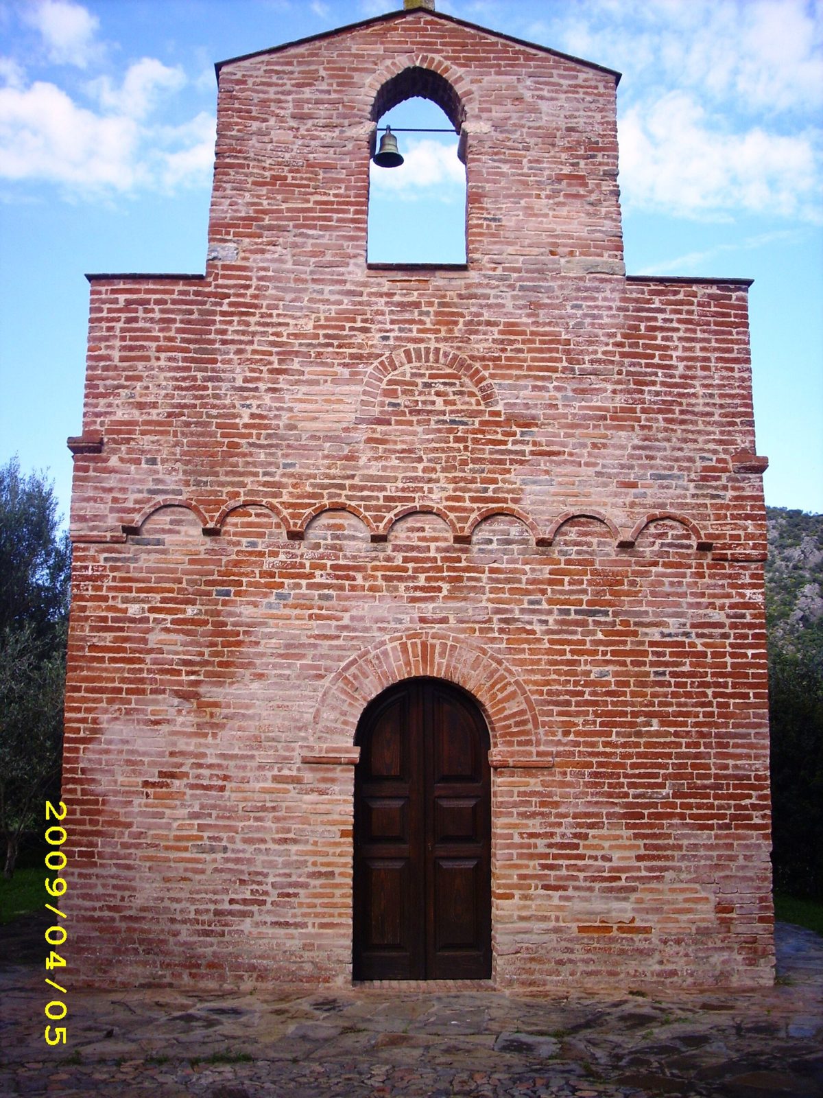 Facciata in mattoni rossi della chiesa romanica di San Nicola di Quirra con campanile a vela